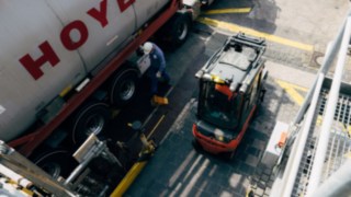 A Linde forklift truck with an explosion-proof design stands next to a tanker with chemicals. A Linde forklift truck with an explosion-proof design stands next to a tanker with chemicals.