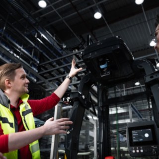 An intralogistics consultant from Linde Material Handling conducts a consultation with a customer in a warehouse environment with an automated vehicle.