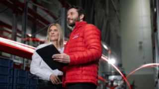 myLinde can be flexibly adapted to the requirements of your company. A man in a red Linde MH jacket and a woman in a white shirt stand in a warehouse and look into the distance.