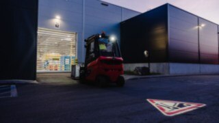 A forklift truck drives towards the roll-up door of a hall at dusk. A forklift truck drives towards the roll-up door of a hall at dusk.