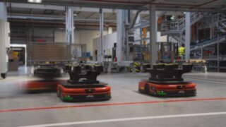 Three autonomous mobile robots (AMRs) from Linde MH drive through the warehouse.