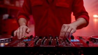 A person in red work clothes is standing at a mixing console.