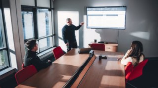 Three people hold a team meeting on intralogistics and automation projects in a meeting room with a presentation on the screen.
