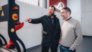 Automation experts exchange ideas in front of a Linde vehicle, symbolising collaborative teamwork, global knowledge exchange and customer-centric automation solutions. 