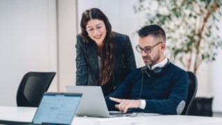 Two employees exchange ideas in front of a laptop, symbolising effective teamwork with a direct impact on the efficiency and sustainability of global supply chains in intralogistics. 