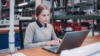 An employee concentrates on her laptop in a workshop environment, symbolising professional development and personal growth at KION Automation.