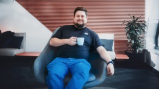 An employee relaxes in an armchair with a cup of coffee in his hand, representing a healthy work-life balance and a positive working environment at KION Automation.