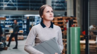 A tech-savvy employee with a laptop under her arm looks focused in a modern warehouse environment as part of Linde's commissioning team. 