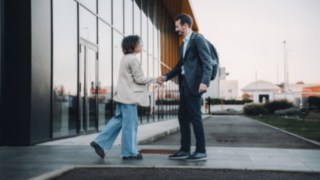 Two international colleagues greet each other in front of the company building, symbolising the global nature of work at KION Automation.