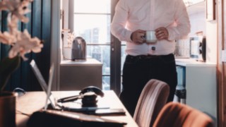 One person works from home with a coffee cup in hand, representing flexible working hours and a healthy work-life balance at KION Automation. 
