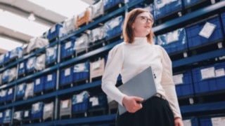 A project manager with a laptop in a modern warehouse is committed to sustainable and efficient supply chains at KION Automation. 