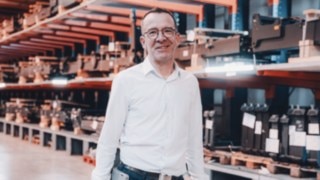 A project manager in light-colored business attire is in a technical warehouse environment, representing the working environment at Linde in the field of automation projects. 