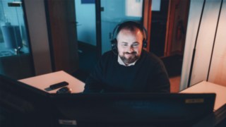 A project manager wearing a headset works at a computer screen, providing insight into everyday work at Linde in the field of intralogistics and automation. 