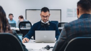 An employee wearing a headset works intently on a laptop in a modern, collaborative office, symbolizing continuous professional development through targeted training and individual support programs.