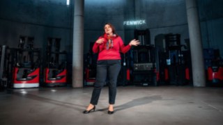 An employee gives a presentation in a modern industrial environment with Linde forklifts in the background, representing international cooperation, intercultural exchange, and global career opportunities in a globally networked company.