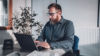 An employee works intently on a laptop in a bright office with natural light, symbolizing flexible working conditions that enable a good work-life balance and productive work in the home office or office.