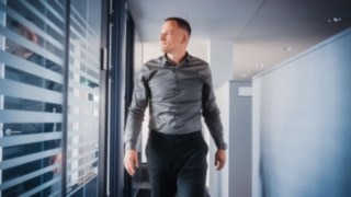 An employee walks confidently through a modern office corridor with glass walls, symbolizing personal responsibility and an active contribution to the efficiency and sustainability of global supply chains.