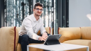 A young sales employee works with a tablet in a modern lounge environment, representing flexible, customer-oriented work in sales and the use of digital tools to present innovative solutions. 