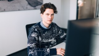 A young KION Automation employee sits focused in front of a monitor at a modern workstation in the office. 